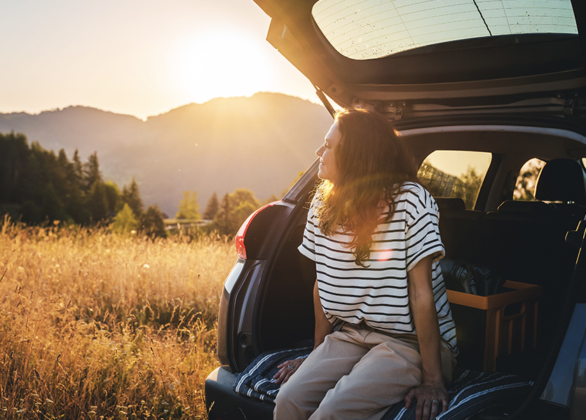Woman sitting on trunk of car looking at sunset