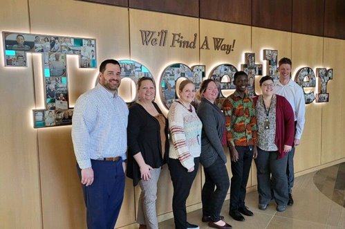 CFCU accounting team with Francis in front of We'll Find A Way Together sign at CFCU's Neenah based headquarters.
