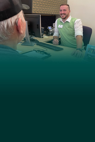CFCU team mate behind desk in green vest helping a member with teal logo overlap.