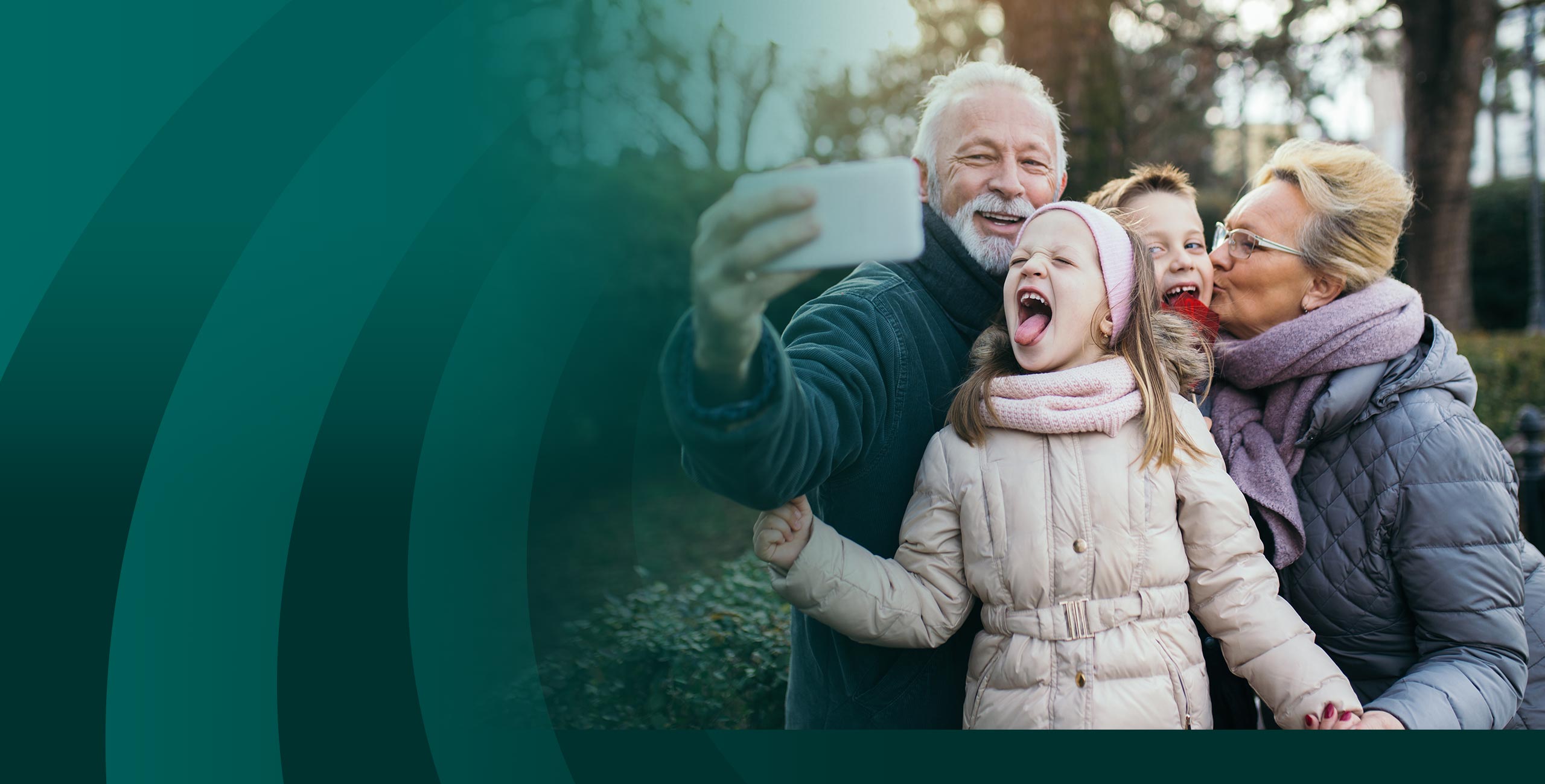 Grandparents taking selfie with boy and girl outdoors.