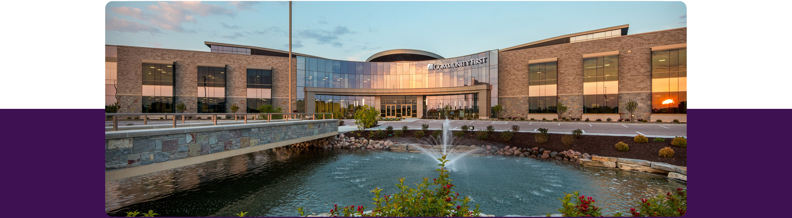 Home office building with glass and brick reflecting sunlight, with flowering plants and fountain in front.