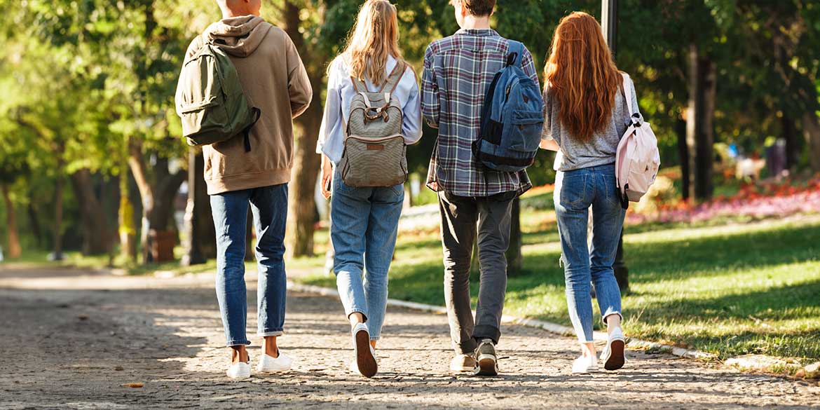 Four college students walking on campus with backpacks