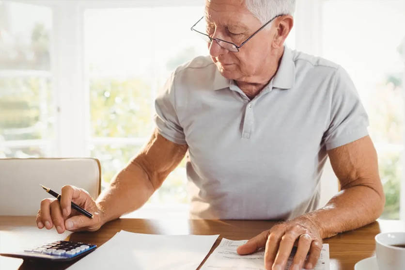 Man in white polo shirt with glasses with calculator, papers, pen, and white coffee cup.