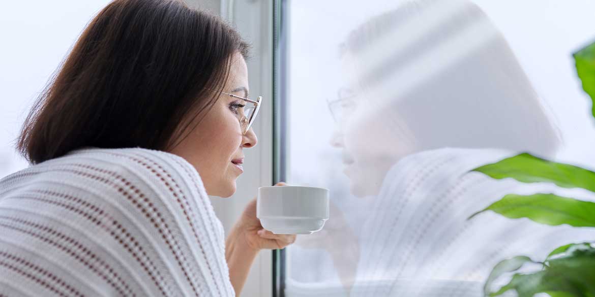 Person with a cup in hand looking out window thinking about investment decisions.