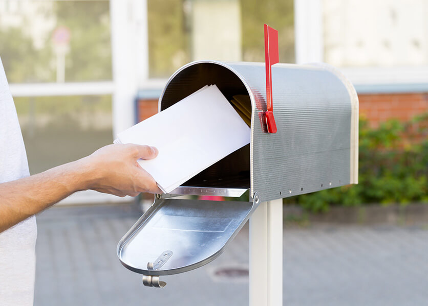 Hand putting white envelope in silver mailbox with red flag up - prevent check fraud.