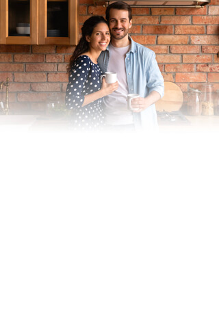 Man in blue shirt and woman in blue polka dot shirt holding coffee cups brick wall.