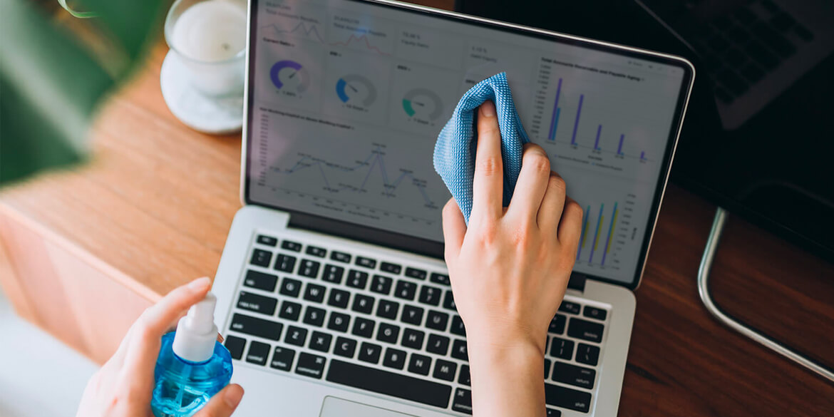 Hands in with blue cloth wiping laptop screen with financial records displaying.