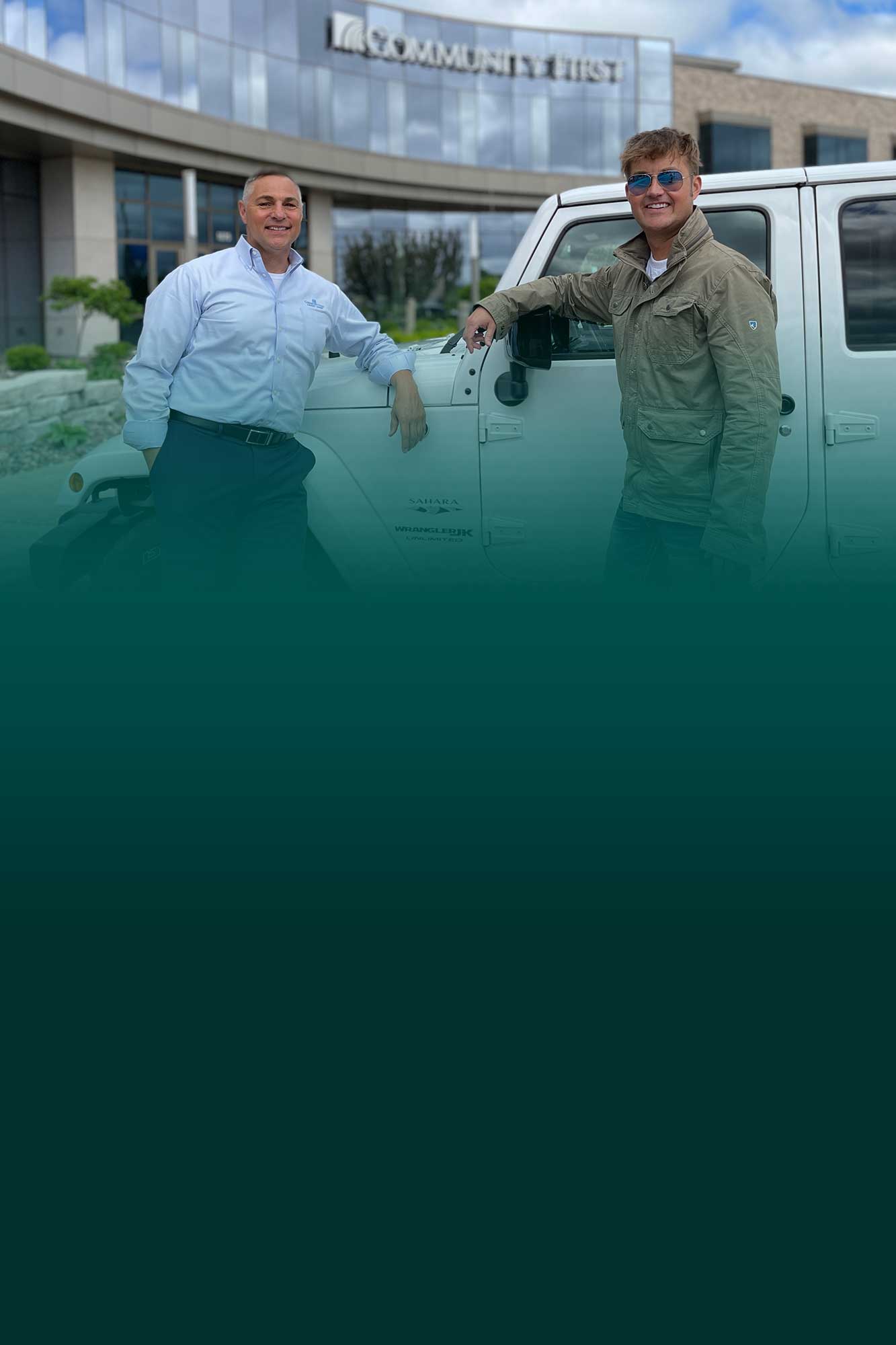 Two men standing in front of a jeep in front of a Community First Credit Union branch having just got a vehicle loan