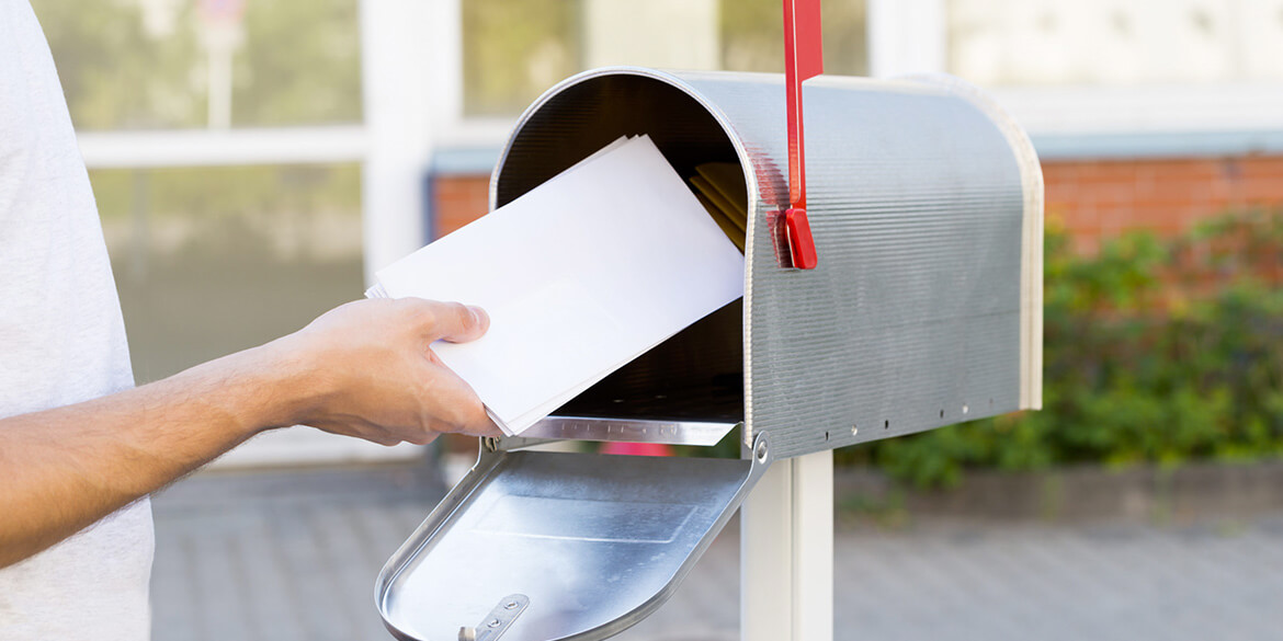 Hand putting white envelope in silver mailbox with red flag up - prevent check fraud.