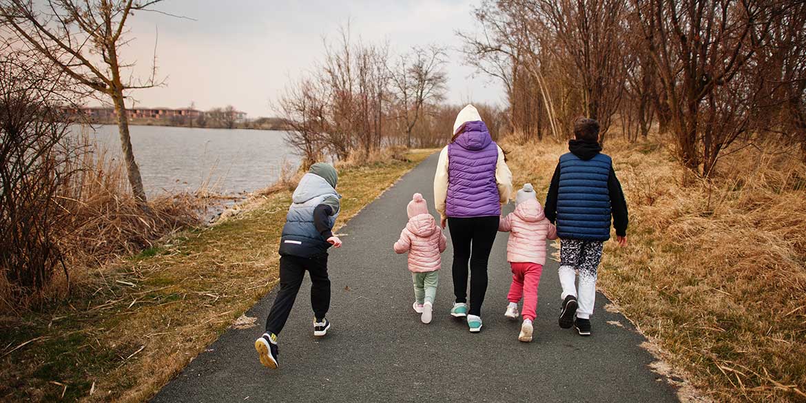Back of woman with kids walking near river.
