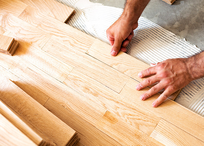 Hands installing blond wood flooring.
