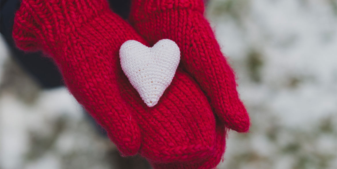 Red crocheted gloves holding a white heart.