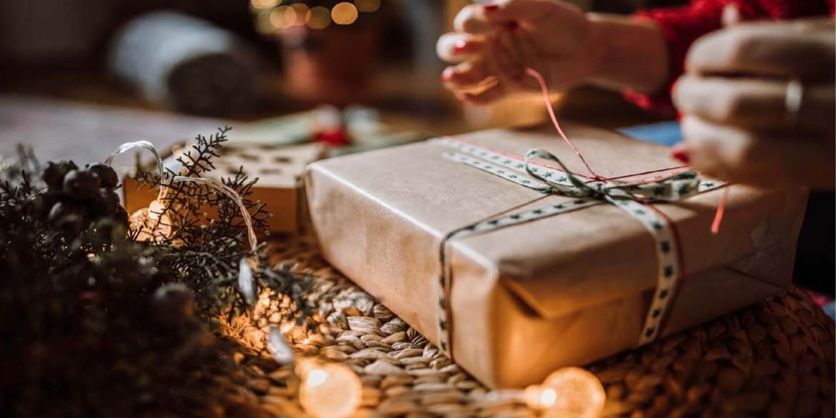 Holiday packaged with someone tying ribbon and lights in background for safe holiday shopping