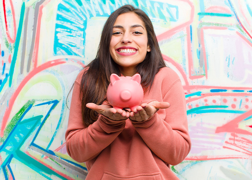 Smiling girl in front of a brightly colored background holding a piggy bank.
