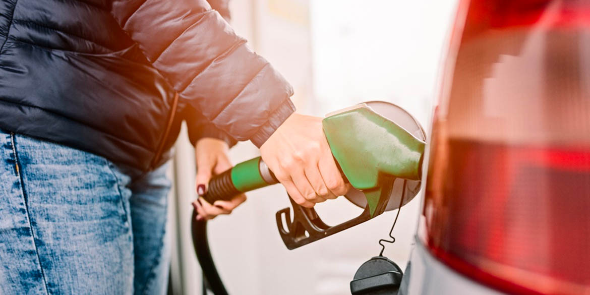 Person with jeans and black jacket pumping gas with green gas nozzle.