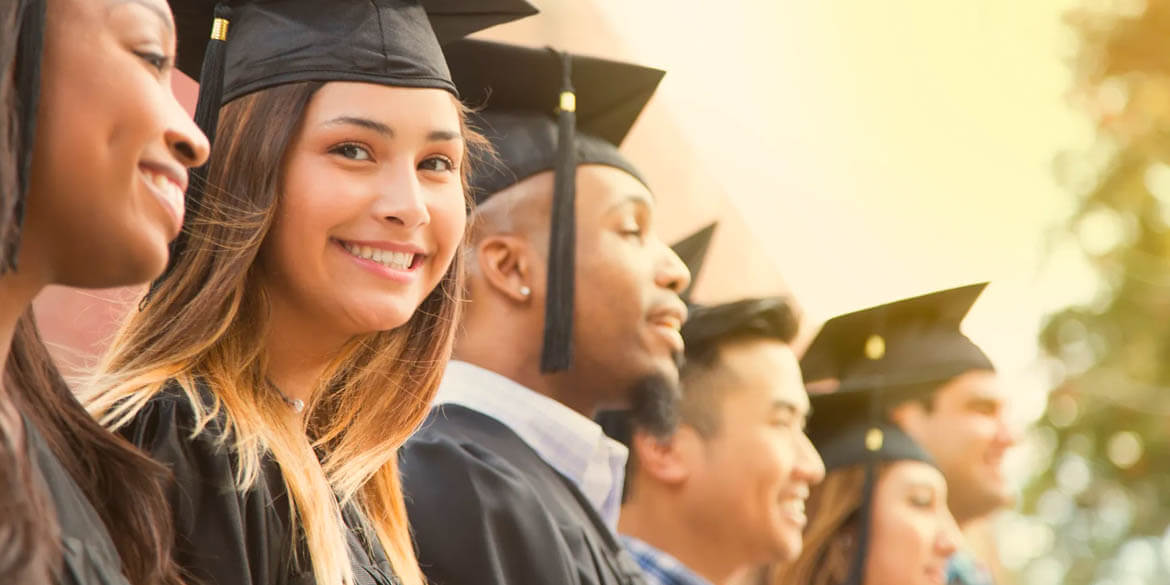 Smiling woman in black graduating cap and gown in crowd.