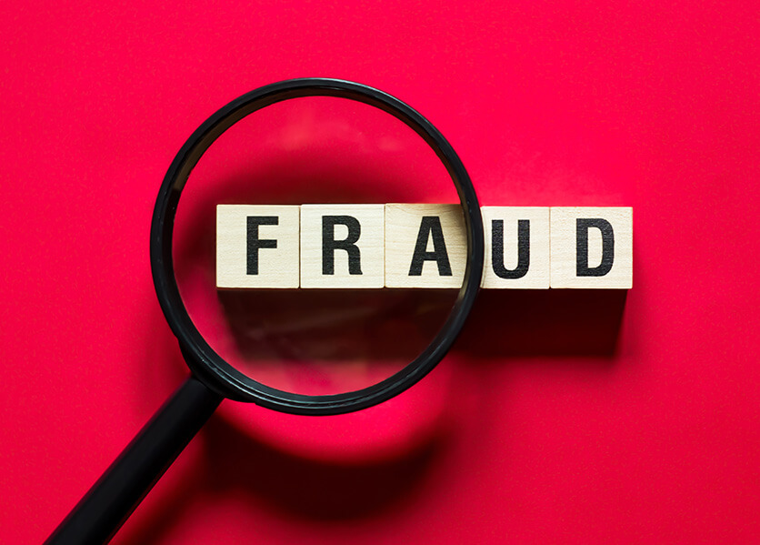 Magnifying glass over the first letters of FRAUD in capital letters on wood blocks.