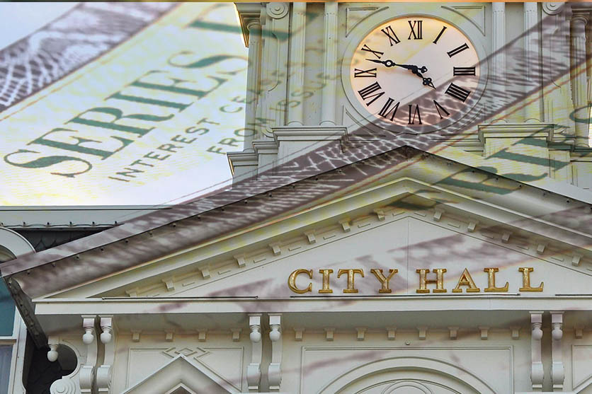 White building with clock tower and City Hall in gold text with dollar bill superimposed.