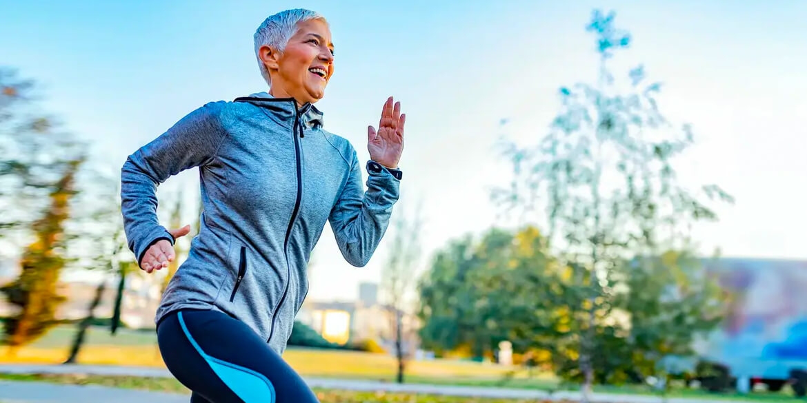 Woman in gray sweatshirt running with trees in background.