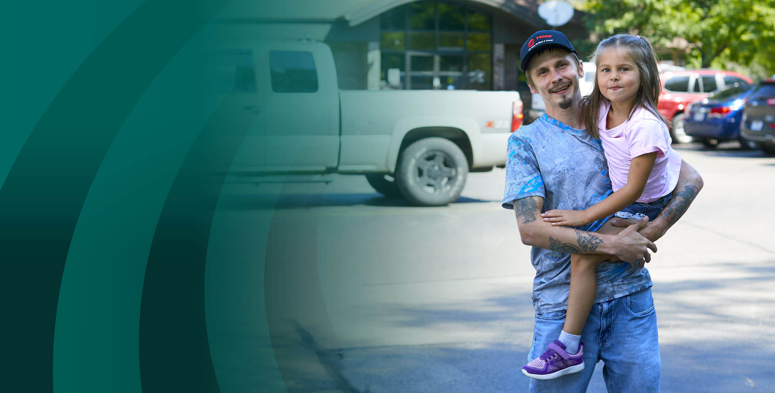 Man holding daughter shopping for truck in front of building with green swirls in background.