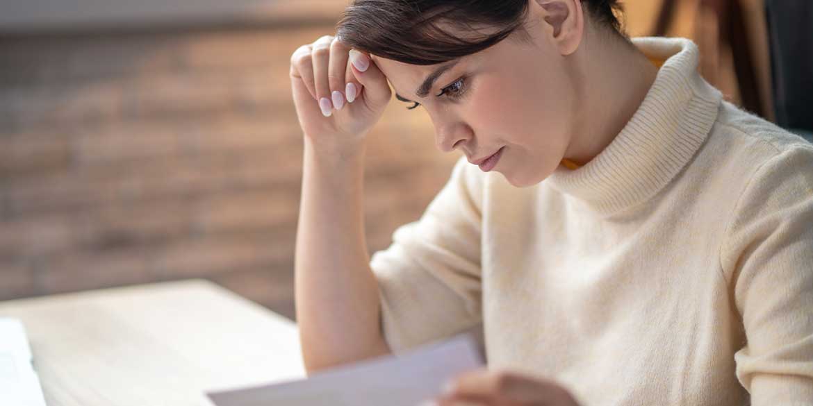 Woman looking pensively at papers as she is reviewing her financial decisions