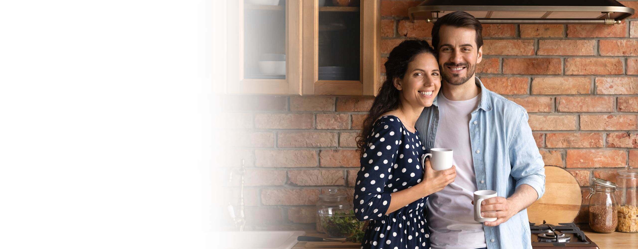Man in blue shirt and woman in blue polka dot shirt holding coffee cups brick wall.