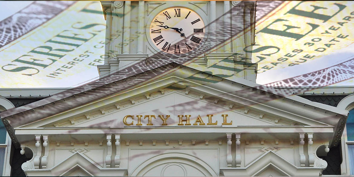 White building with clock tower and City Hall in all caps, gold text with dollar bill superimposed on top of building.