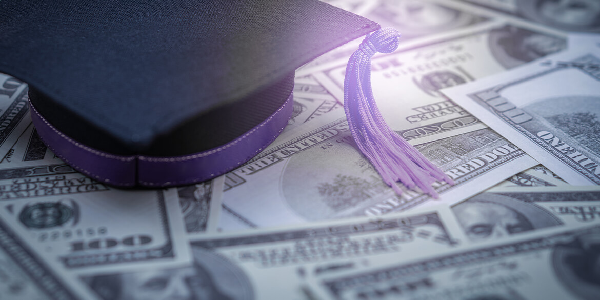 A graduation cap with tassle sitting on money spread out to signify students getting scholarships