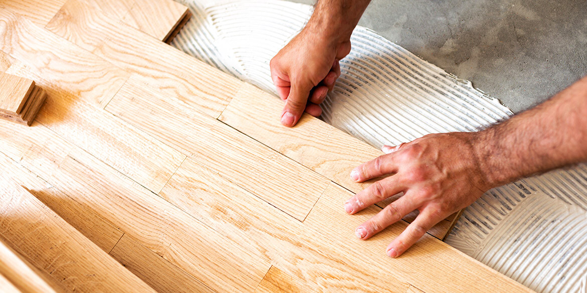 Close up of hands installing blond wooden floor.