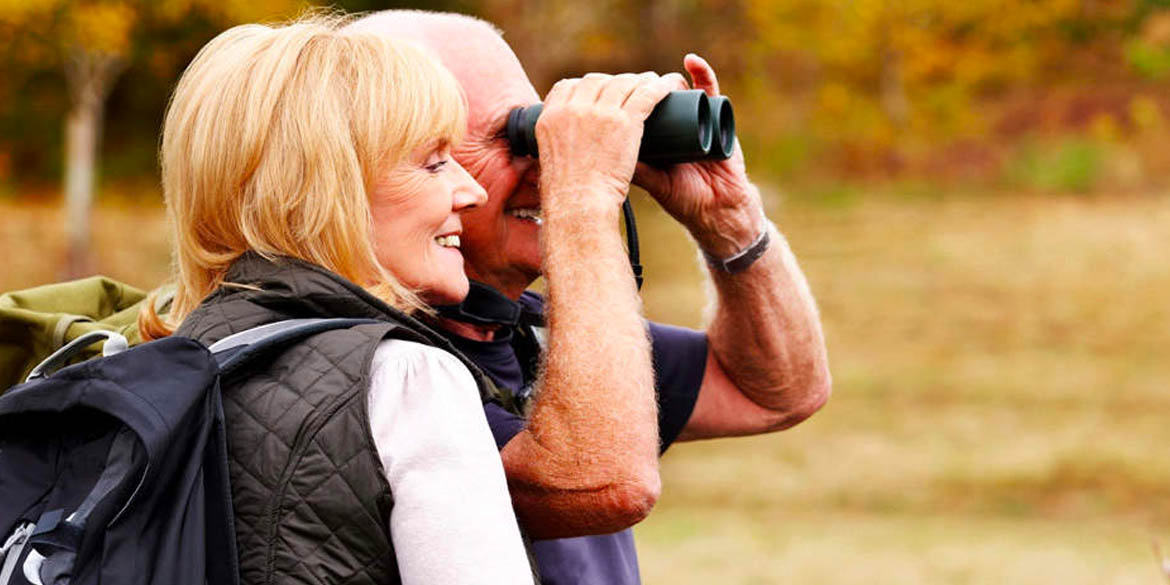 Man and woman looking through binoculars outside.
