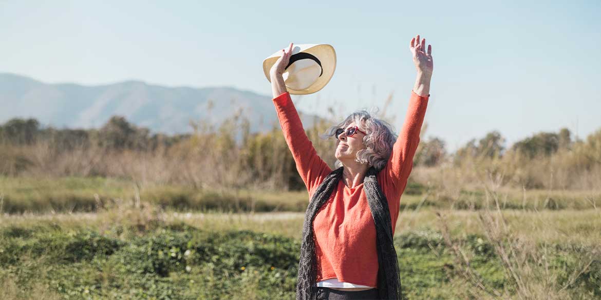 Woman with hat raising arms in the mountains.