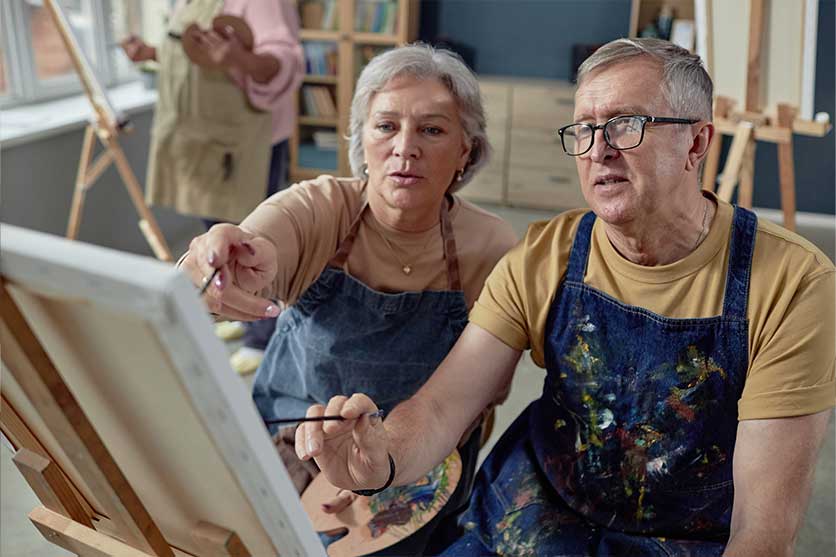 Couple painting in blue aprons enjoying retirement.