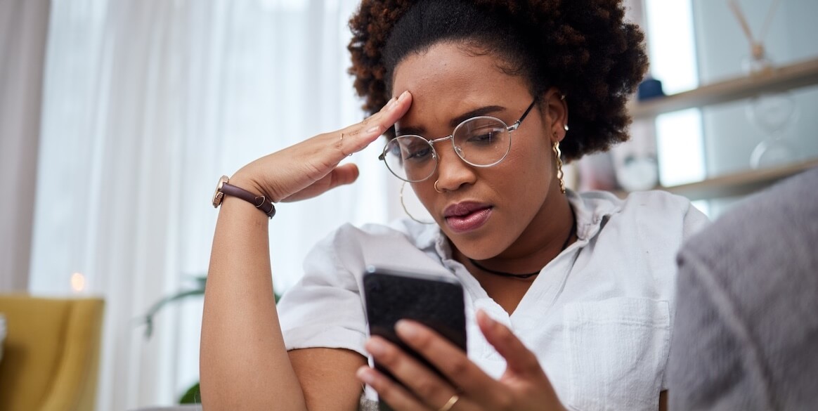 Woman stressed reading message from scammer on phone.