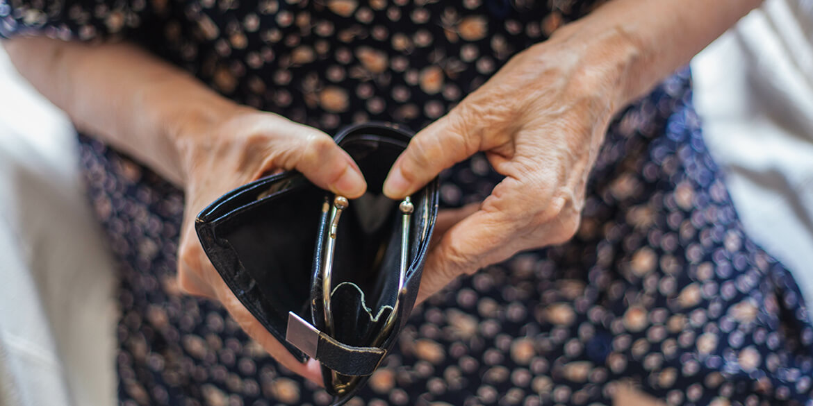 Elderly hands holding black empty wallet indicating elder fraud.