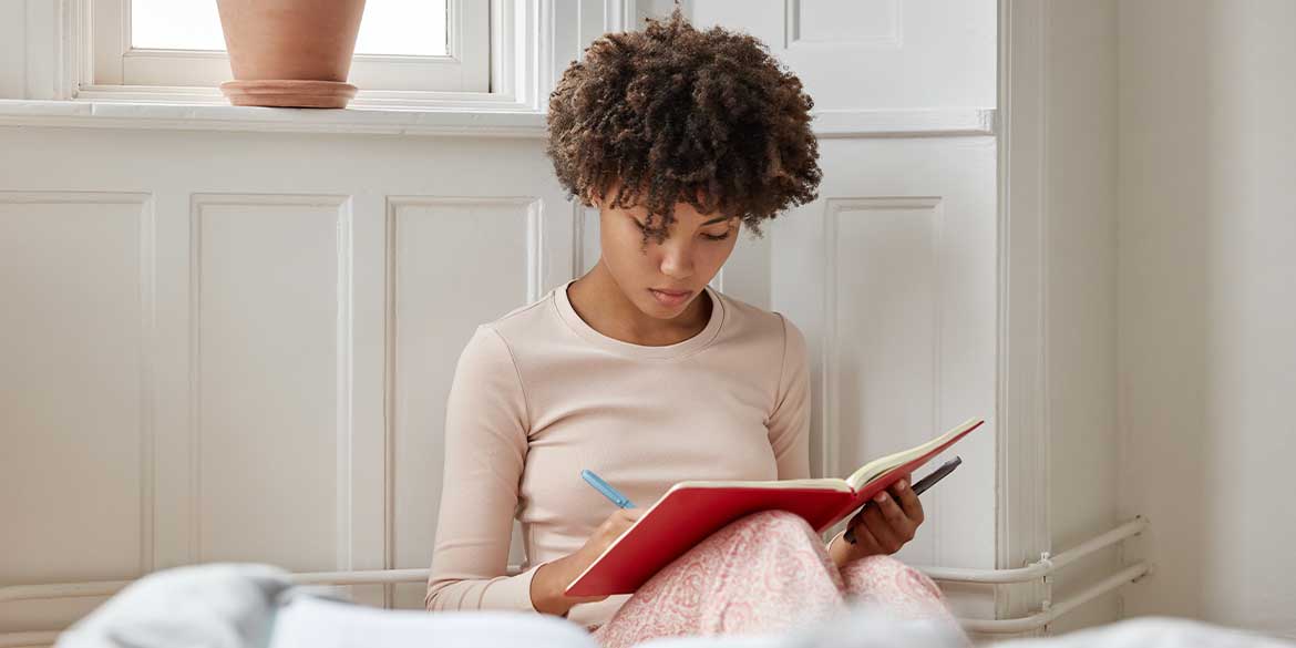 Woman in pink writing in red journal.