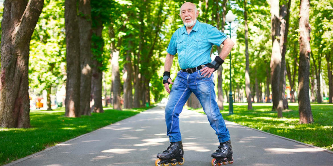 Man in teal shirt with blue jeans and roller blades with trees in background.