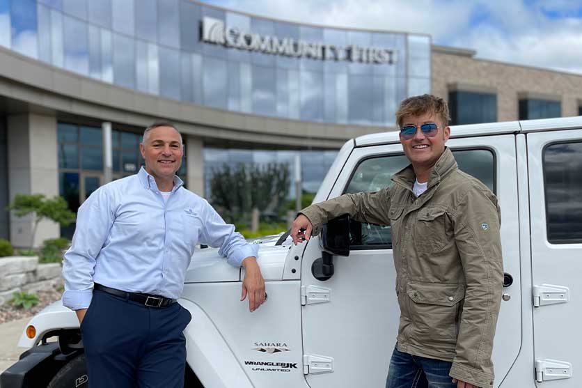 Two men in front of a jeep in front of a Community First Credit Union branch just getting a loan for the car.