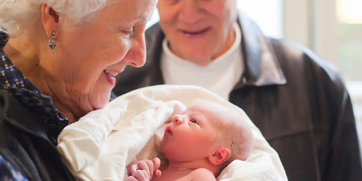 Grandma and grandpa in black shirts holding newborn baby.