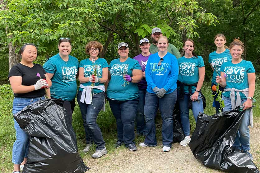 Group of CFCU employees pose for portrait outdoors as they were picking up trash for their community