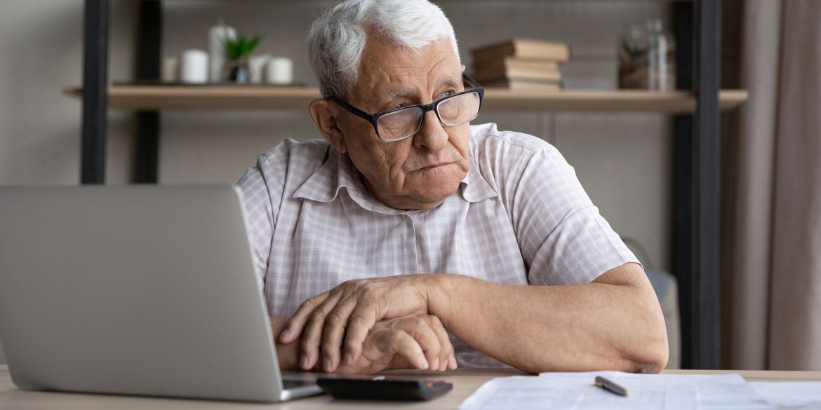 An older gentleman looking worried in front of a computer showing financial exploitation