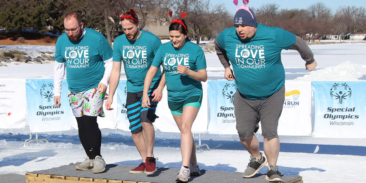 Four People in Blue Shirts Jumping into Water for 2023 Special Olympics Polar Plunge