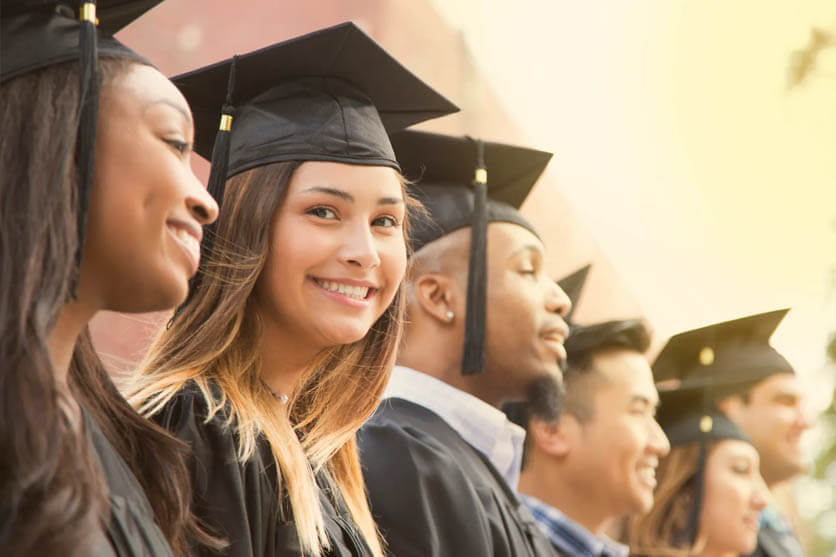 Smiling woman in black graduating cap and gown in crowd.